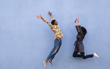 Black couple jumping outdoor with blue wall in background - Crazy happy african friends having fun...