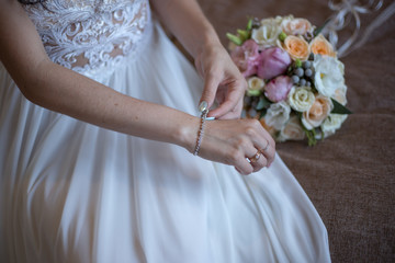 Obraz na płótnie Canvas bride in a white dress puts on a bracelet