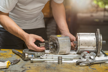 Professional mechanic man inspection hydraulic gear pump of wheel loader in workshop, repair...