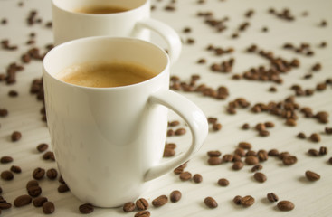 Two white coffee cups on a wooden table with copy space and scattered grains