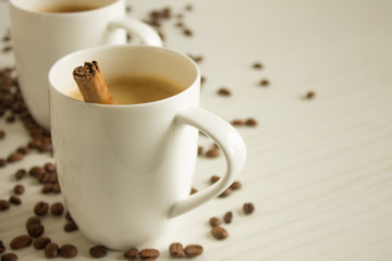 Two white coffee cups with a cinnamon stick on a wooden table with copy space and scattered grains