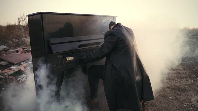 man in leather clothes and gas mask playing a smoking piano on the street