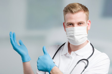 Doctor with medical face mask and medical gloves shows thumbs up