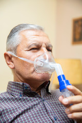 Senior man using medical equipment for inhalation with respiratory mask, nebulizer