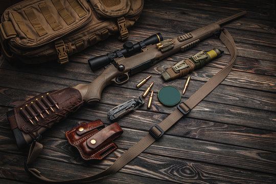 Modern bolted carbine and cartridges for it on a dark wooden table. Rifle with a telescopic sight on a dark backg. Weapons for hunting, sports and self-defense. Postcard concept.