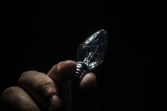Cropped Image Of Person Holding Light Bulb Against Black Background