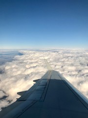 Fototapeta na wymiar High up in the stratosphere, close to heaven: Above the white clouds on a scenic journey in an airplane flight of a vacation journey seeing the aircraft wing gliding over the bright cloudscape