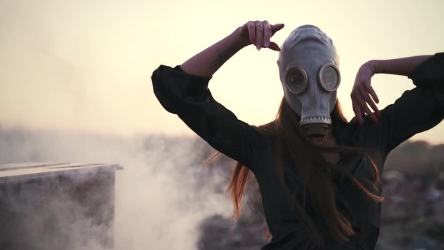 girl in a black dress, pantyhose and gas mask dancing near a smoking piano in a junkyard