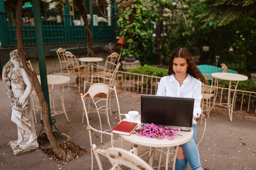 A beautiful young girl with a laptop, a book and flowers sitting in the garden