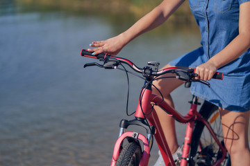 Close-up, a red bike with a girl on a background of water. Bike walk in nature.