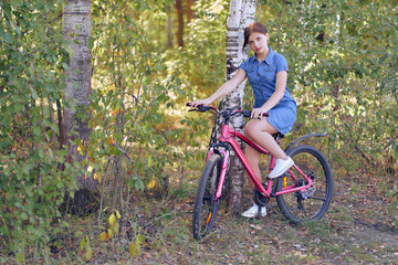 Naklejka premium A student sitting in a blue dress on a female bike on nature in a birch forest.