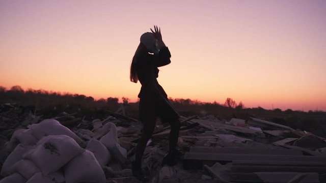 girl in a black dress, in tights and a gas mask dancing at sunset on the ruins