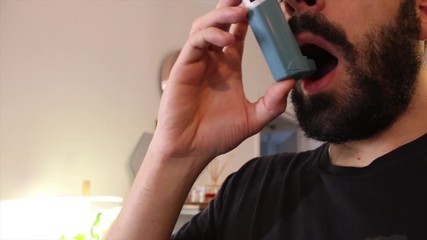 Young man blue shirt using blue asthma inhaler for relief asthma attack. Pharmaceutical products is used to prevent and treat wheezing and shortness of breath caused asth - Powered by Adobe