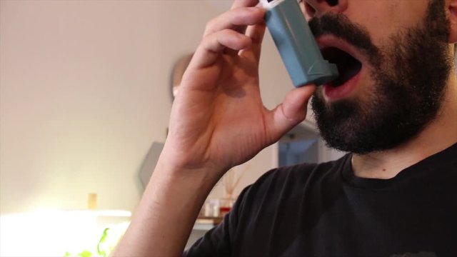 Young man blue shirt using blue asthma inhaler for relief asthma attack. Pharmaceutical products is used to prevent and treat wheezing and shortness of breath caused asth