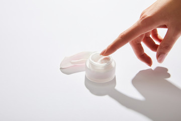 Cropped view of female hand with cosmetic cream in glass jar on grey background