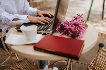 A beautiful young girl with a laptop, a book and flowers sitting in the garden