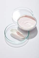 High angle view of laboratory glassware with cosmetic cream and rose petal on grey background