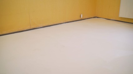 Worker puts primer with roller on concrete floor in room from unfinished apartment. Repair in the...