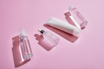 High angle view of cosmetic hand cream tube, cosmetic bottle, spray and serum bottle with liquid on pink background