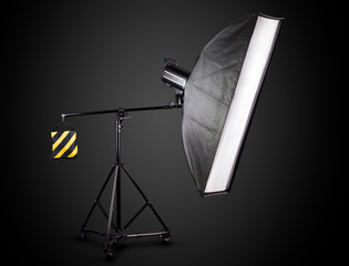 Photo studio lighting stands with flash and softbox isolated on the black.