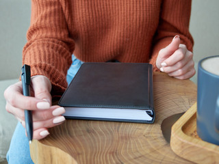 the girl's hands are holding a dark leather planner and a fountain pen. close up. wooden table