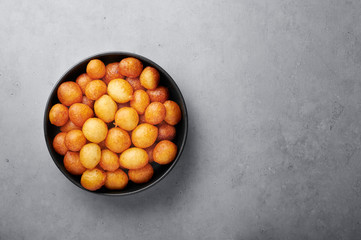 Loukoumades or luqaimat or lokma in black bowl on grey concrete background. Loukoumades is eastern cuisine donunts popular during Ramazan. Popular Ramadan Food. Iftar and Suhur sweets