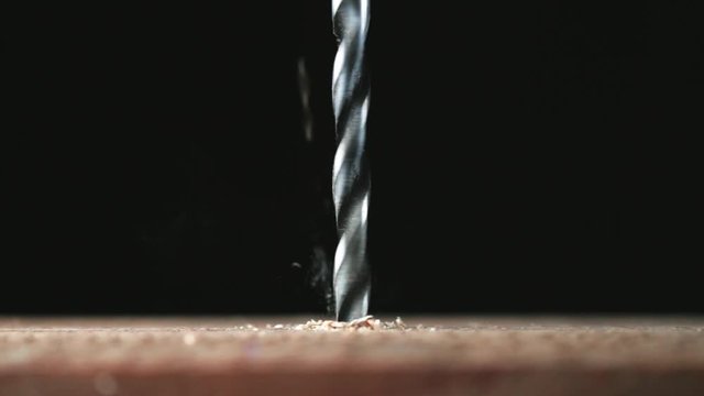 Electric drill bit drills a hole in the board. Joinery and construction work close up. Wood chippings fly off a metal drill. Handyman bores holes into a wooden board.  