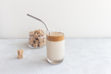 Dalgon coffee delicious cold drink in a glass cup with a metal straw on a light background with cane sugar cubes. Trend.