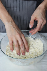 The cook's hands knead the dough in a large glass bowl. Homemade cake. Housework.