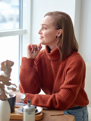 a positive girl in a brown jacket is sitting at a table in a cafe and holding a pen. Reverie.