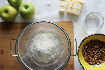 Preparations for Apple pie: flour, apples, butter, nuts. Homemade cake.
