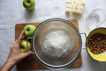 Preparations for Apple pie: flour, apples, butter, nuts. Homemade cake.