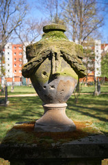 Ancient stone memorial urn showing the signs of world war 2, ridden with bullet holes, standing in one of the oldest cemetaries of Berlin.