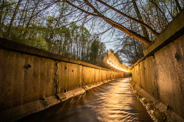 A stream in a concrete ditch or rainwater channel at night in forest with flying lighting warm light (freezelight). Storm drainage in the evening.