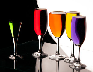 five glasses with multicolor liquid on reflection surface with white and black background