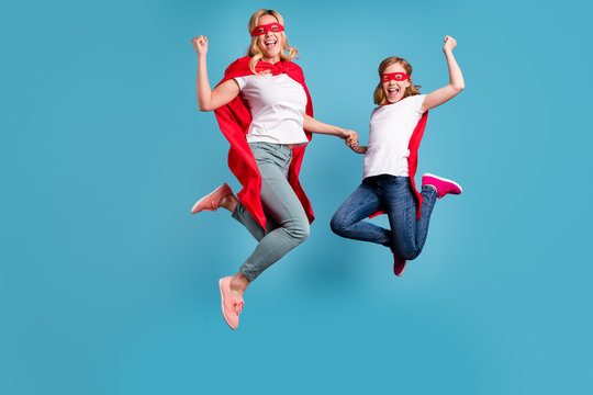 Full Length Photo Of Funny Mom Lady Little Daughter Spend Time Together Superhero Win Costume Competition Jump High Up Wear S-shirts Red Coat Masks Isolated Blue Color Background