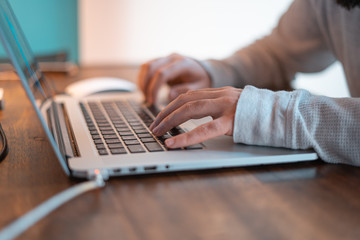 Hands pictured on the keyboard of a laptop typing something. 