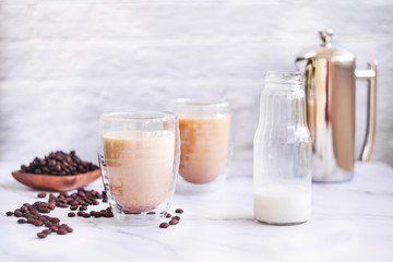 Fresh poured white cooffee with milk in front of french press pot and scattered cooffee beans