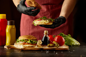 The chef prepares a burger, a hamburger on a black table with ingredients. Delicious and fast food, fast food. A menu, a cafe, fast food, catering, gastronomy