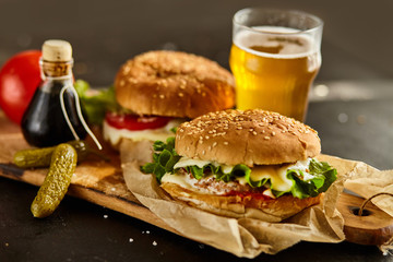Homemade beef burgers with a glass of beer, tomatoes, cheese, sauce on wooden cutting board