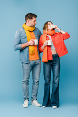 ill couple in scarves holding cups with hot drinks while woman sneezing on blue