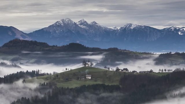 Zoom out time lapse of famous Saint Thomas church on hilltop with moving fog. In background Alps mountains. Amazing landscape nature in Slovenia. Well known spot for photographers all around the world