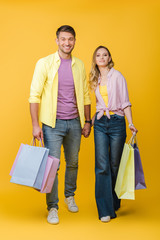 cheerful couple holding shopping bags on yellow