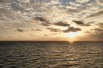 Breathtaking sunset in the middle of the ocean, with yellow orange blue sky and white clouds, View from the deck of cruise ship. Travel vacation voyage landscape.