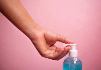 Close up hand holding alcohol gel bottle on pink pastel background.