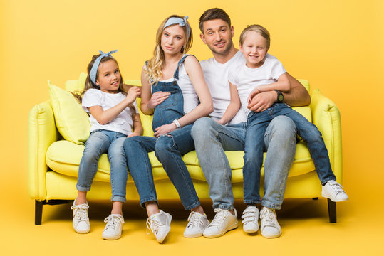 happy pregnant mother, father and children sitting on sofa on yellow