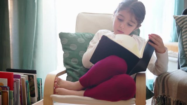 happy little girl reading a book sitting at home, concept of leisure at home for children
