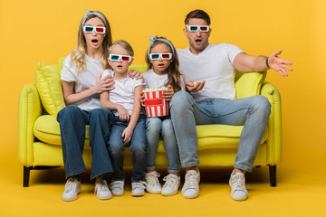 shocked family in 3d glasses watching movie on sofa with popcorn bucket on yellow