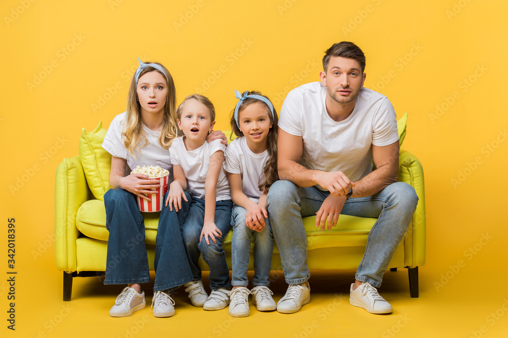 Wall mural surprised family watching movie on sofa with popcorn bucket on yellow - Wall murals