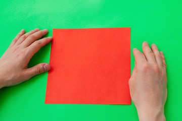 Men's hands fold a heart from red paper in the origami technique on a green background.Step-by-step instructions, step 1.Gift concept for Valentine's day, mother's day